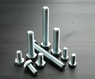 Photo of Metal bolts on dark wooden table, closeup
