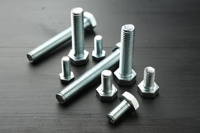 Photo of Metal bolts on dark wooden table, closeup