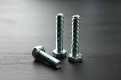 Photo of Metal bolts on dark wooden table, closeup