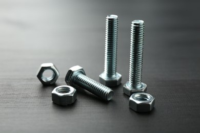 Photo of Metal bolts and hex nuts on dark wooden table, closeup