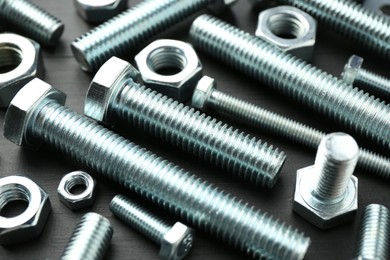 Photo of Metal bolts and hex nuts on dark wooden table, closeup