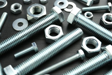 Photo of Metal bolts and hex nuts on dark wooden table, closeup