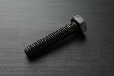 Photo of One metal bolt on dark wooden table, closeup