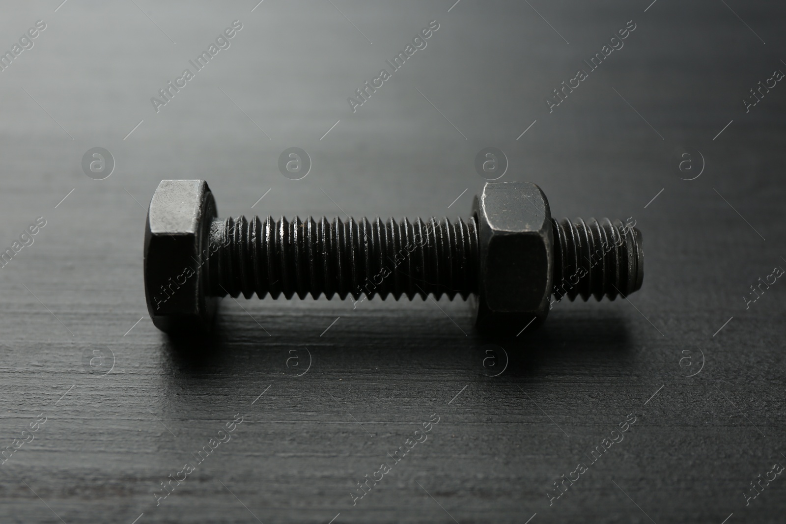 One metal bolt on dark wooden table, closeup Photo of One metal bolt on dark wooden table, closeup