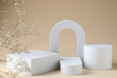 Photo of Promotion. Podiums for product presentation and gypsophila flowers on beige background, closeup