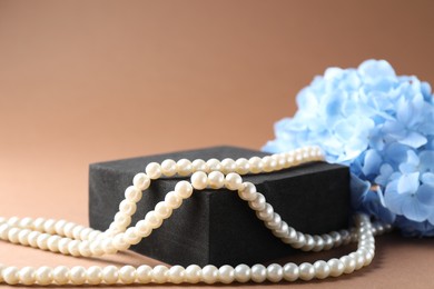 Photo of Promotion. Pearl jewelry, podium and hydrangea flowers on brown background, closeup
