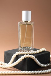 Photo of Promotion. Bottle of perfume, pearl jewelry and podium on brown background, closeup