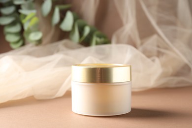 Photo of Promotion. Jar of cosmetic product, tulle cloth and green leaves on brown background, closeup