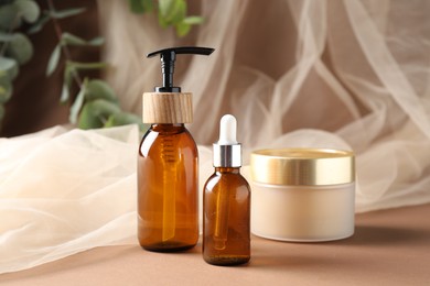 Photo of Promotion. Different cosmetic products, tulle cloth and green leaves on brown background, closeup