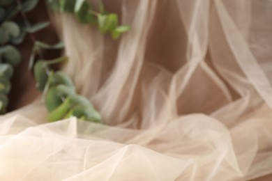 Photo of Promotion. Tulle cloth and green leaves on brown background, closeup
