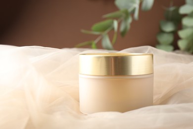 Photo of Promotion. Jar of cosmetic product, tulle cloth and green leaves on brown background, closeup