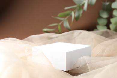 Photo of Promotion. Podium for product presentation, tulle cloth and green leaves on brown background, closeup