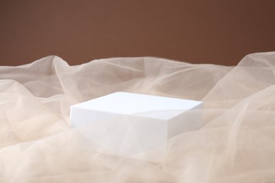 Photo of Promotion. Podium for product presentation and tulle cloth on brown background, closeup