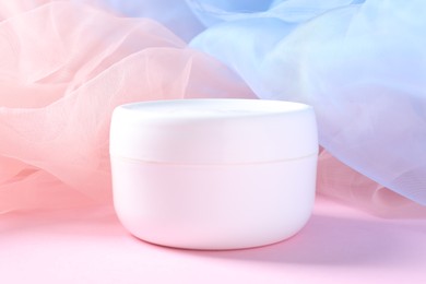 Photo of Promotion. Jar of cosmetic product and tulle cloth on pink background, closeup