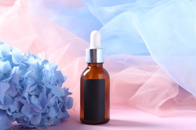 Photo of Promotion. Bottle of cosmetic product, hydrangea flowers and tulle cloth on pink background
