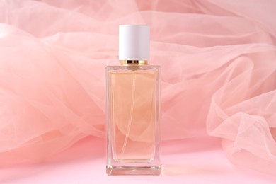 Photo of Promotion. Bottle of perfume and tulle cloth on pink background, closeup