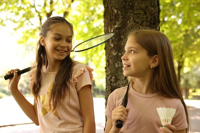 Photo of Smiling little girls with badminton rackets and shuttlecock near tree in park