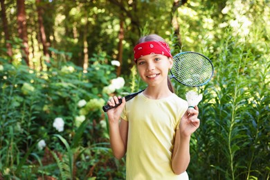 Photo of Portrait of smiling little girl in bandana with badminton racket and shuttlecock in park