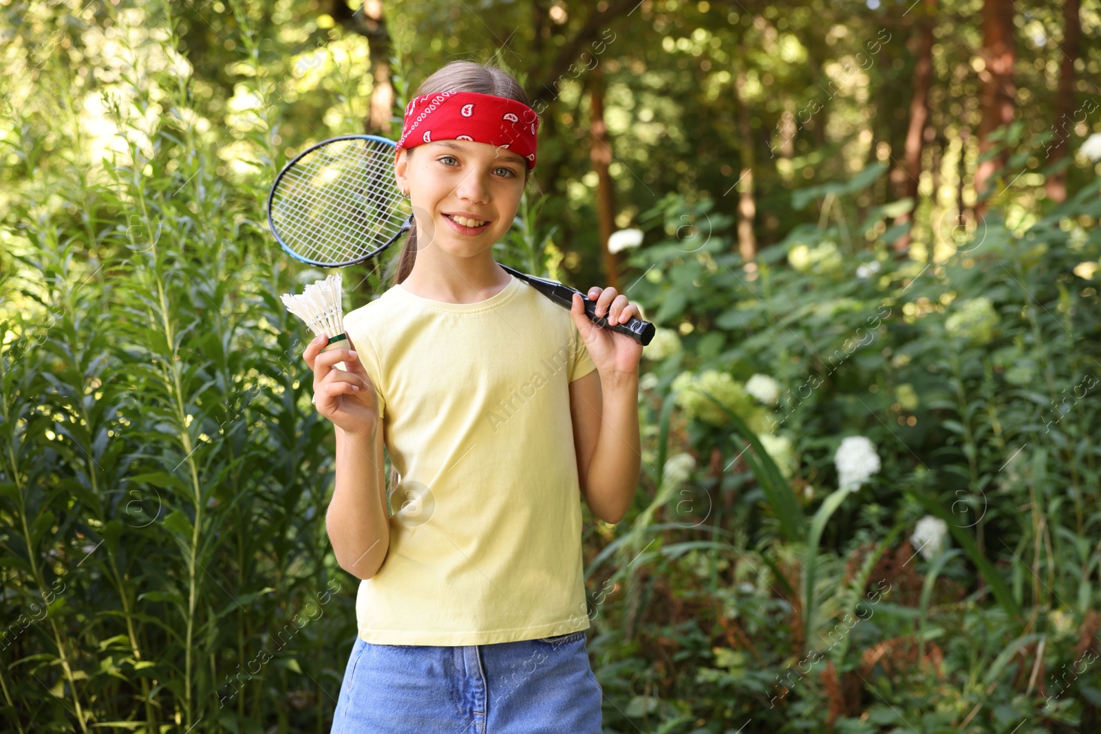 Portrait of smiling little girl in bandana with badminton racket and shuttlecock in park Photo of Portrait of smiling little girl in bandana with badminton racket and shuttlecock in park