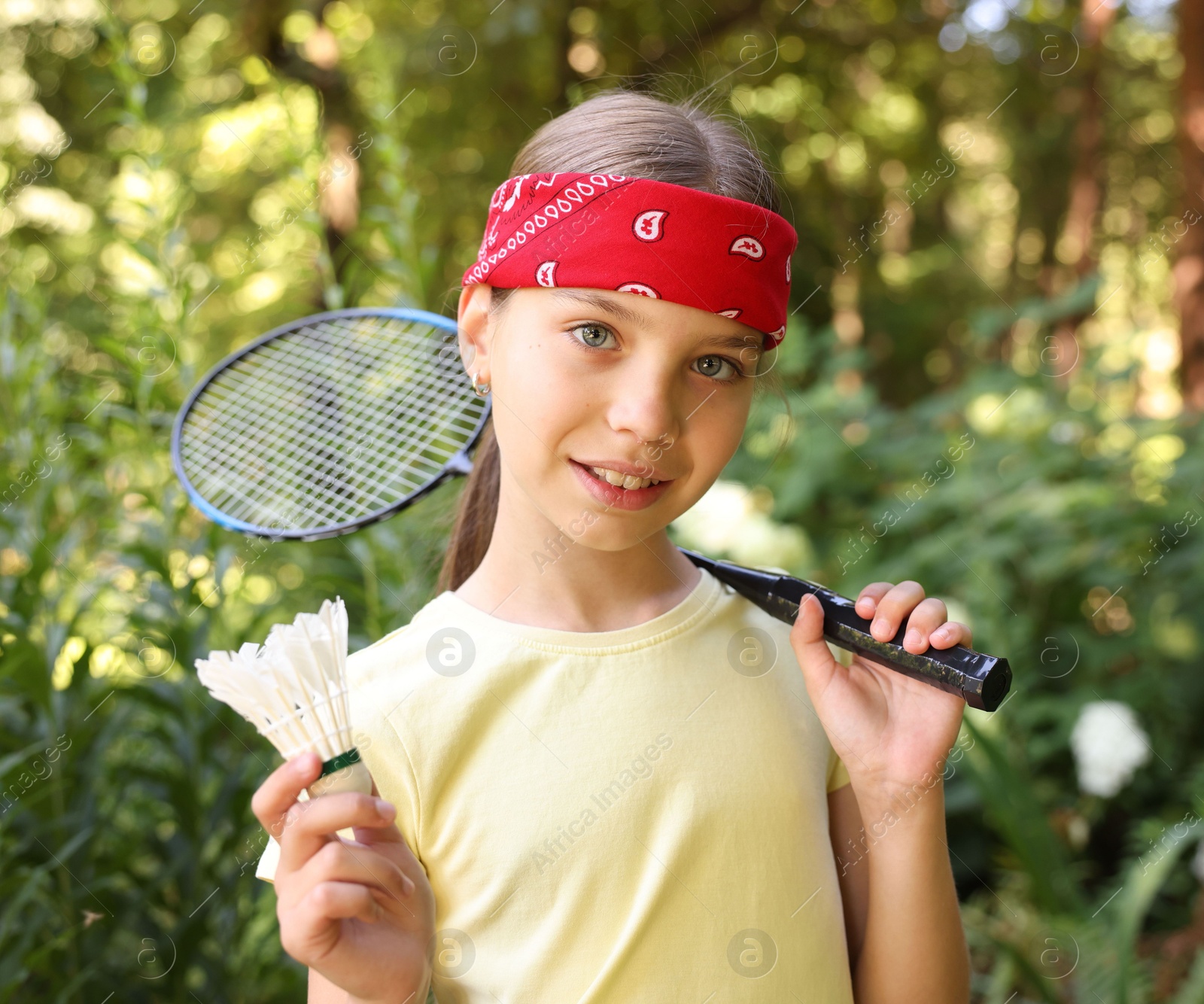 Portrait of smiling little girl in bandana with badminton racket and shuttlecock in park Photo of Portrait of smiling little girl in bandana with badminton racket and shuttlecock in park
