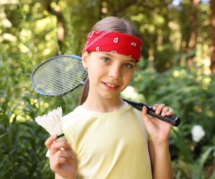 Photo of Portrait of smiling little girl in bandana with badminton racket and shuttlecock in park