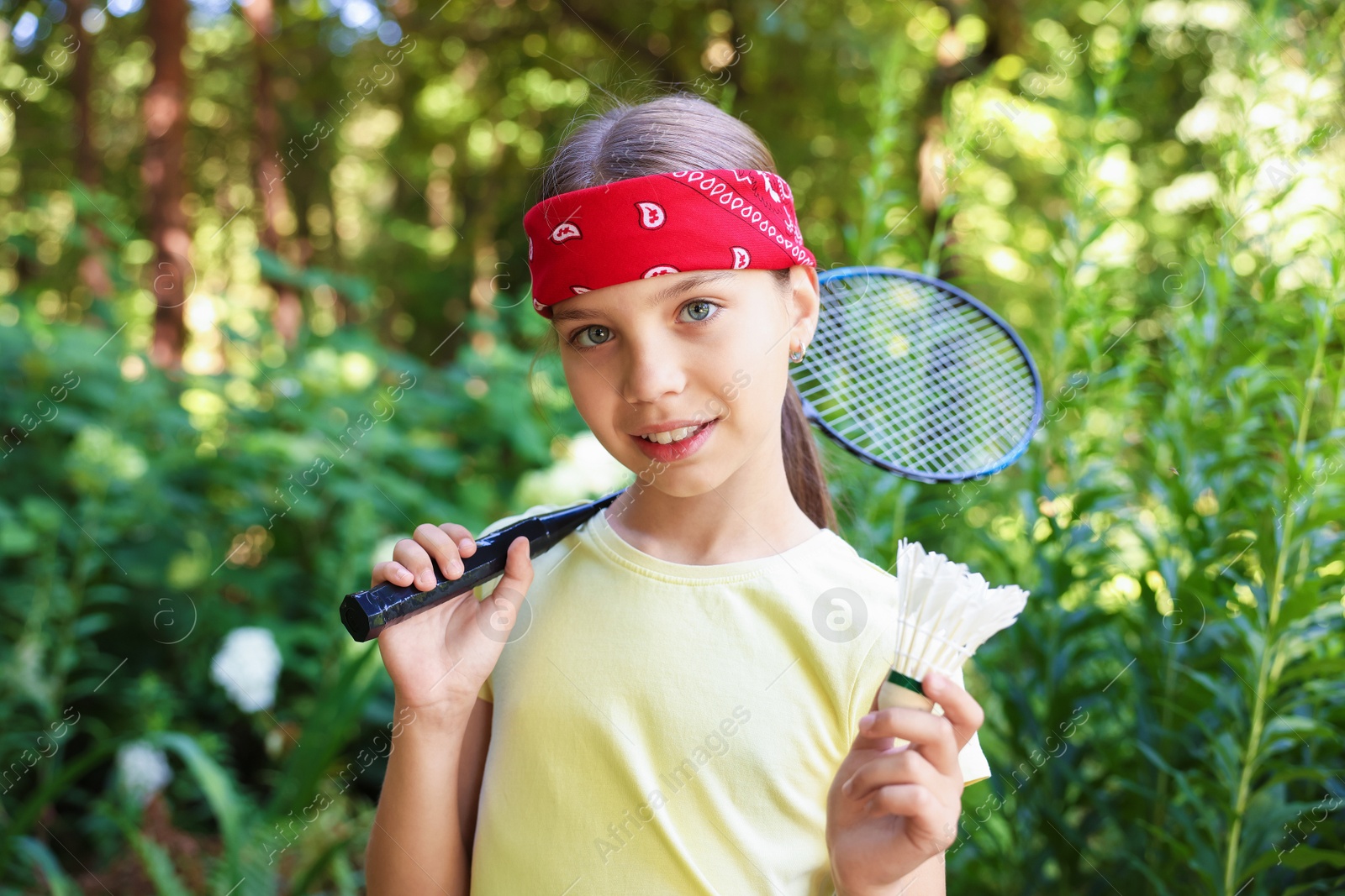 Portrait of smiling little girl in bandana with badminton racket and shuttlecock in park Photo of Portrait of smiling little girl in bandana with badminton racket and shuttlecock in park