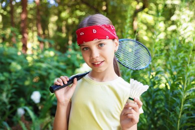 Photo of Portrait of smiling little girl in bandana with badminton racket and shuttlecock in park