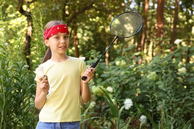 Photo of Portrait of smiling little girl in bandana with badminton racket and shuttlecock in park