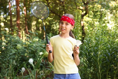 Photo of Portrait of smiling little girl in bandana with badminton racket and shuttlecock in park