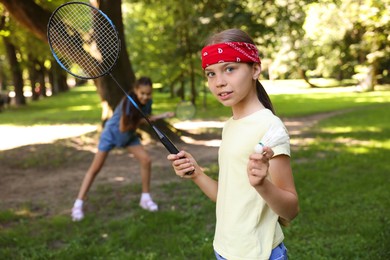 Photo of Cute little girl in bandana with badminton racket and shuttlecock playing with her friend in park, selective focus