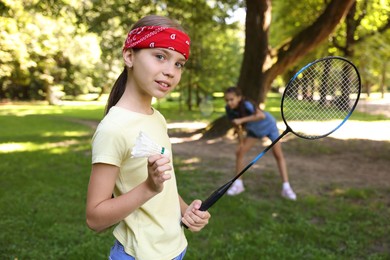 Photo of Smiling little girl in bandana with badminton racket and shuttlecock playing with her friend in park, selective focus