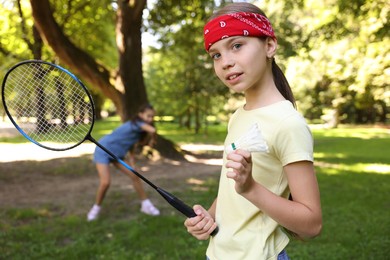 Photo of Smiling little girl in bandana with badminton racket and shuttlecock playing with her friend in park, selective focus