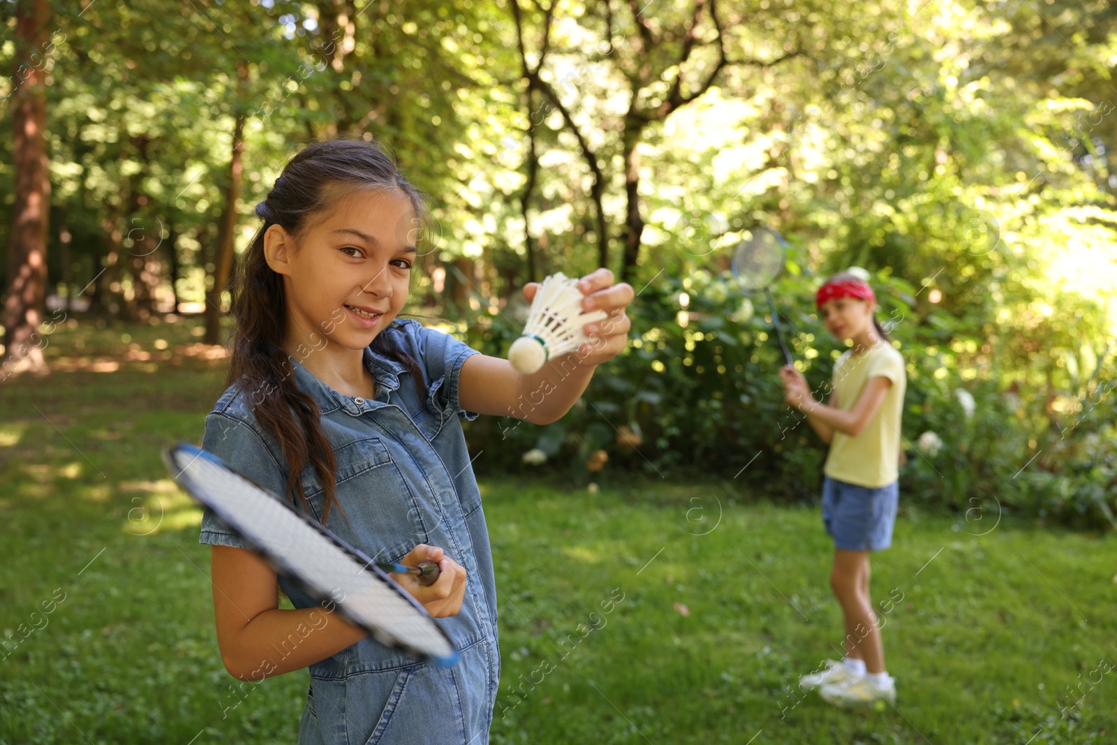 Smiling little girl with badminton racket and shuttlecock playing with her friend in park, selective focus Photo of Smiling little girl with badminton racket and shuttlecock playing with her friend in park, selective focus