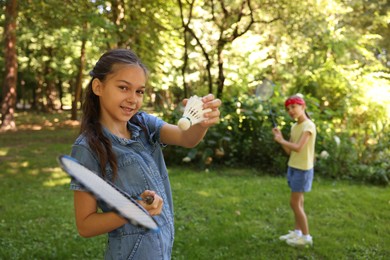 Photo of Smiling little girl with badminton racket and shuttlecock playing with her friend in park, selective focus