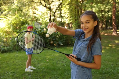 Photo of Smiling little girl with badminton racket and shuttlecock playing with her friend in park, selective focus