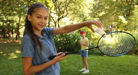 Photo of Smiling little girl with badminton racket and shuttlecock playing with her friend in park, selective focus
