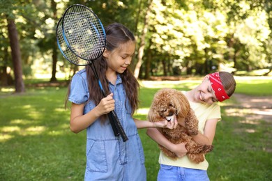 Photo of Smiling little girls with badminton rackets having fun with their dog in park