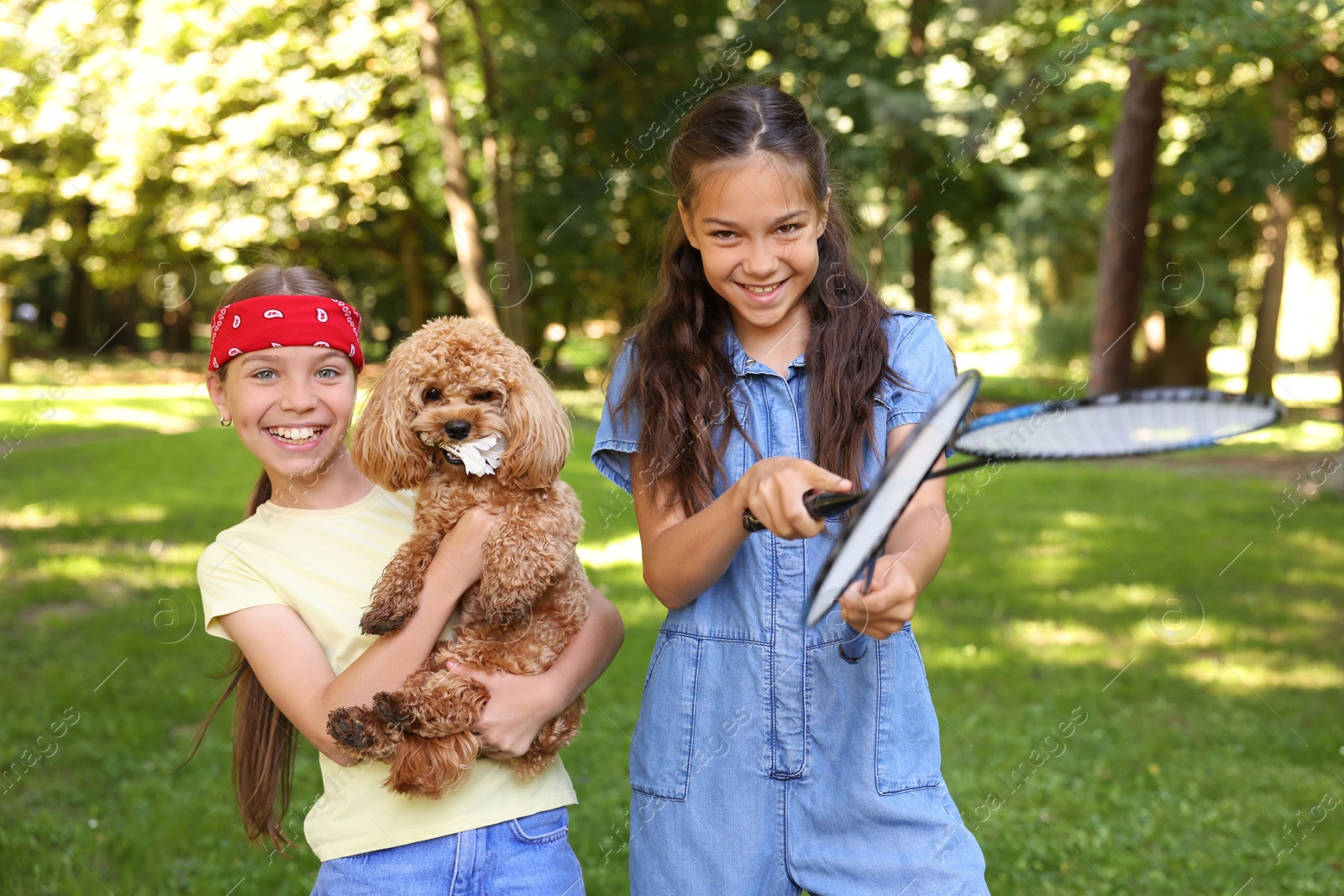 Smiling little girls with badminton rackets having fun with their dog in park Photo of Smiling little girls with badminton rackets having fun with their dog in park