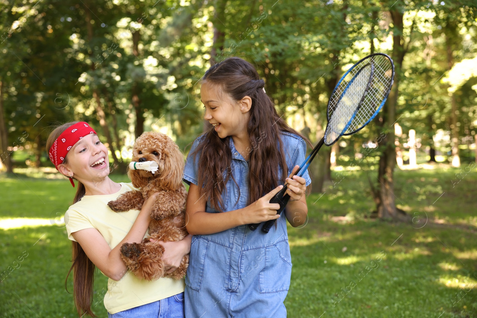 Smiling little girls with badminton rackets having fun with their dog in park Photo of Smiling little girls with badminton rackets having fun with their dog in park