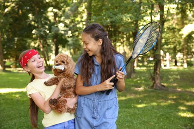Photo of Smiling little girls with badminton rackets having fun with their dog in park