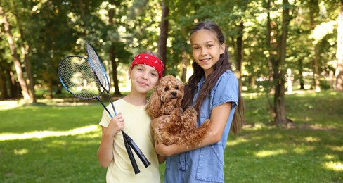 Photo of Portrait of cute little girls with badminton rackets and dog in park