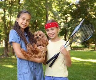 Photo of Portrait of cute little girls with badminton rackets and dog in park