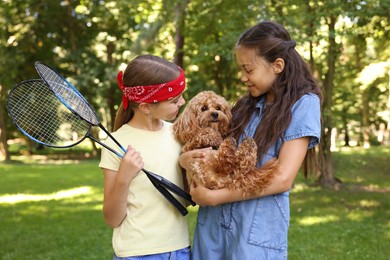 Photo of Cute little girls with badminton rackets and dog in park