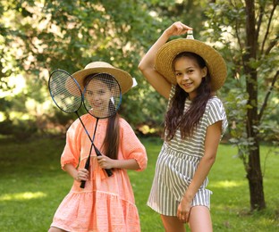 Photo of Portrait of smiling little girls in hats with badminton rackets and shuttlecock in park