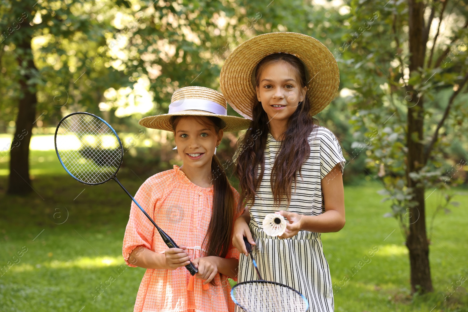 Portrait of smiling little girls in hats with badminton rackets and shuttlecock in park Photo of Portrait of smiling little girls in hats with badminton rackets and shuttlecock in park