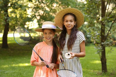 Photo of Portrait of smiling little girls in hats with badminton rackets and shuttlecock in park