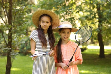 Photo of Portrait of smiling little girls in hats with badminton rackets and shuttlecock in park