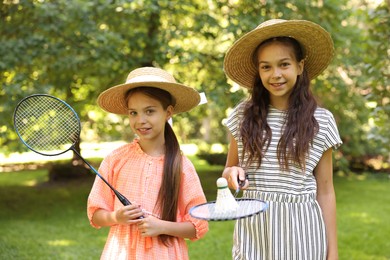 Photo of Portrait of smiling little girls in hats with badminton rackets and shuttlecock in park