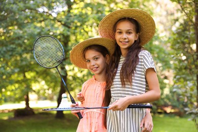 Photo of Portrait of smiling little girls in hats with badminton rackets and shuttlecock in park