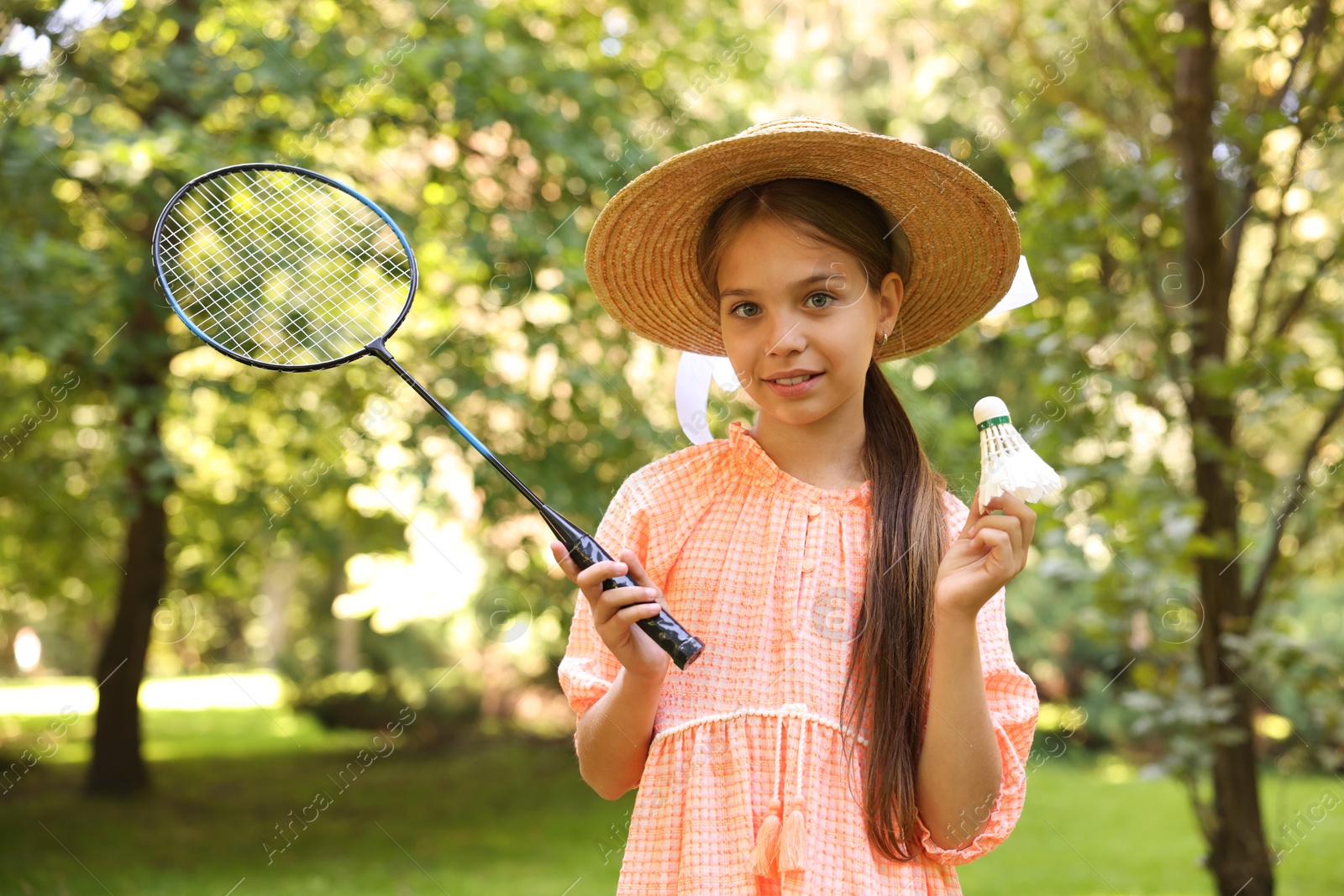 Portrait of smiling little girl in hat with badminton racket and shuttlecock in park Photo of Portrait of smiling little girl in hat with badminton racket and shuttlecock in park